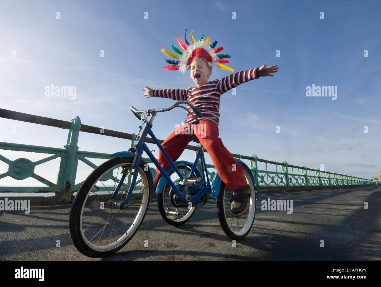 Ein kleiner Junge in einem Indianer Kopfschmuck schreien, wie er auf einem Trike auf den Fahrradweg auf Brighton Seafront spielt Stockfoto