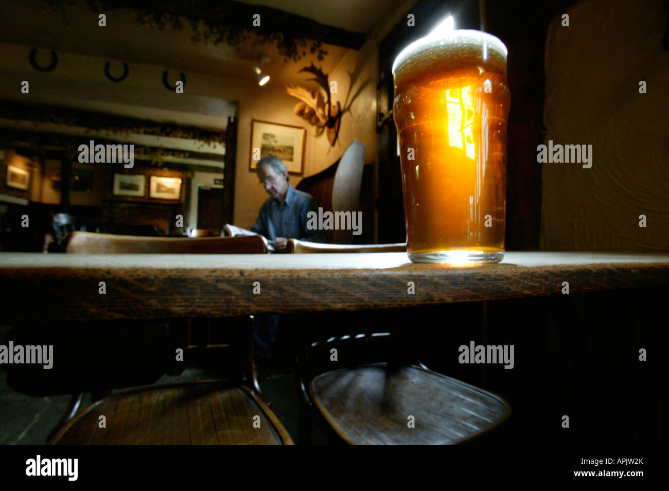 Ein Pint bitter stehend auf einem alten Holztisch in einem englischen Pub. Ein Mann sitzt an einem Tisch hinter. Stockfoto