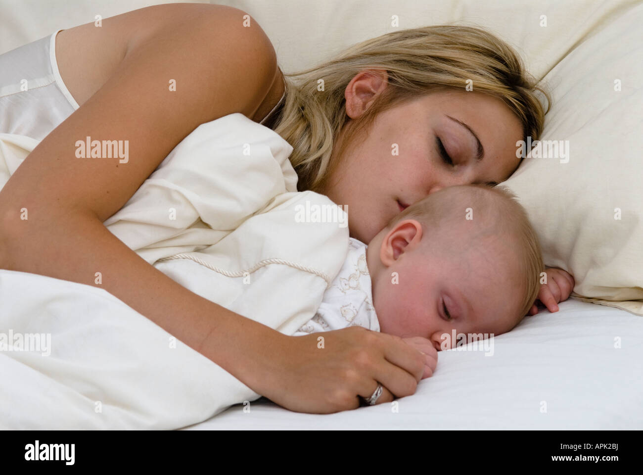 Junge im Bett, der mit dem Gesicht nach unten in den Armen der schlafenden Mutter schläft, fünf Monate alt Stockfoto
