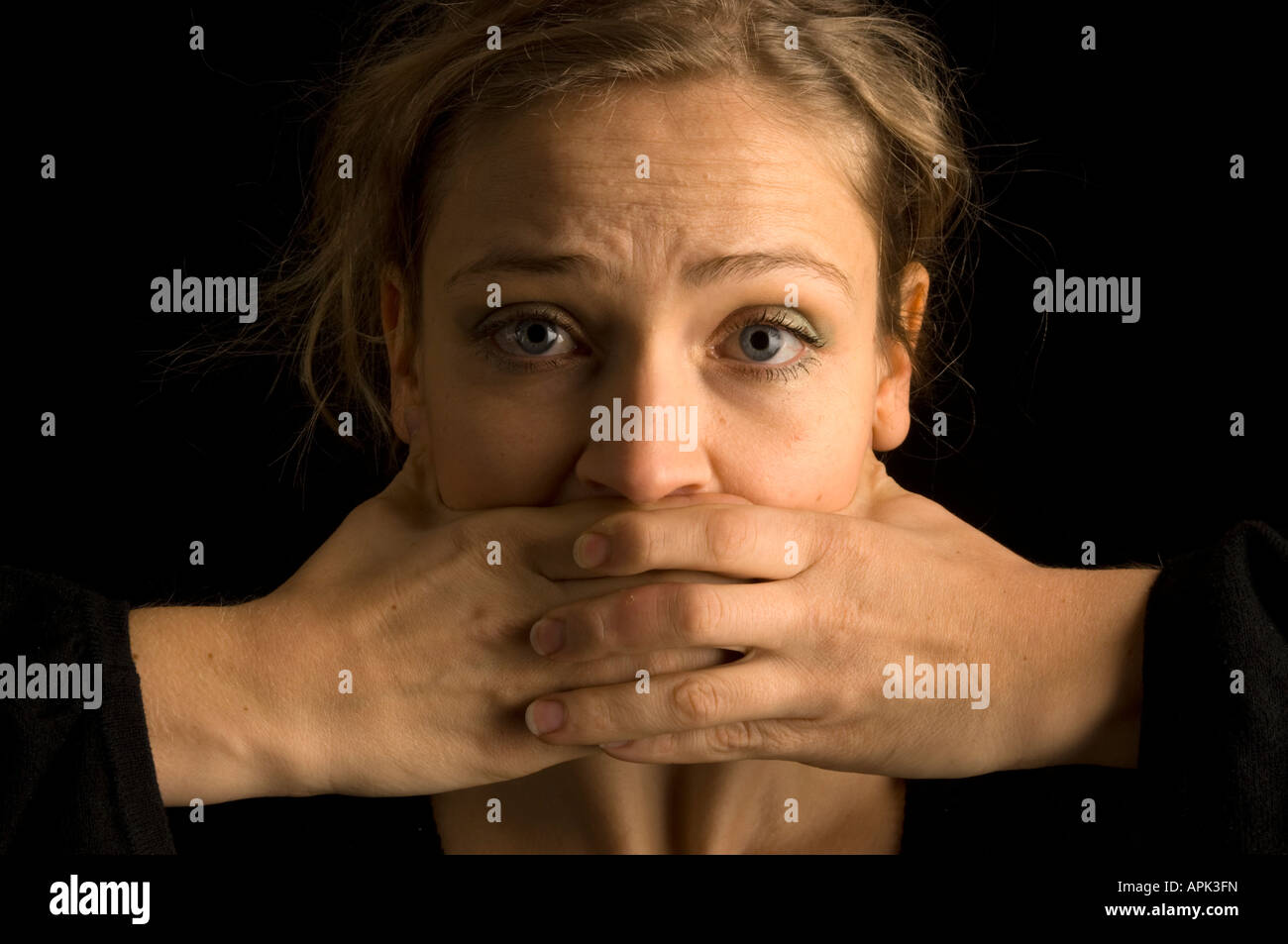 junge blonde Frau mit Hand vor den Mund im Studio vor schwarzem Hintergrund - Konzept der Zensur & Kontrolle darüber sprechen Stockfoto