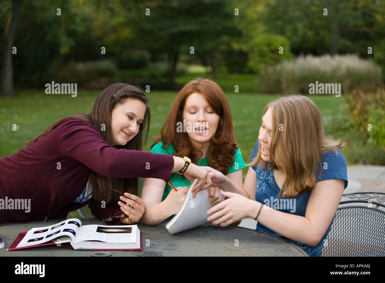 ILLINOIS Riverwoods drei Mädchen im Teenageralter goofing um anstatt zu studieren zusammen Lehrbuch öffnen auf Tabelle Stockfoto