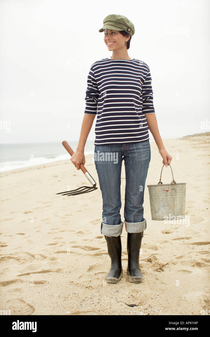 Frau mit Eimer und Heugabel stehen am Strand. Stockfoto