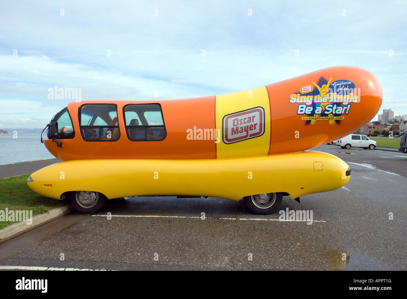Die Kraft Heinz Foods Company sponsert ein oranges und gelbes Hot Dog-förmiges Wienermobile, das in der Nähe von Wasser unter bewölktem Himmel parkt. Stockfoto