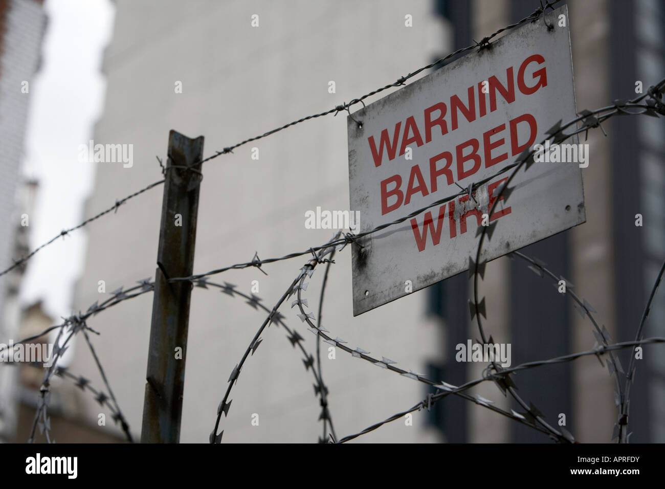 Warnung Stacheldraht Schild zu Stacheldraht befestigt und Stacheldraht auf einem Zaun umliegenden Gebäuden Belfast Nordirland Vereinigtes Königreich Stockfoto