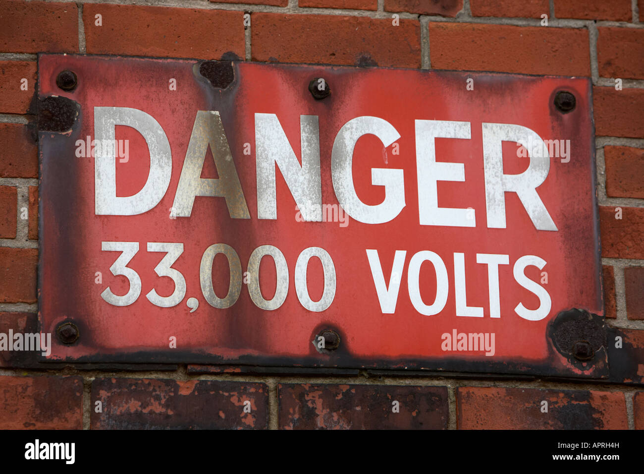 alten verwitterten verrosteten Gefahr, dass 33000 Volt Warnzeichen angebracht, ein roten Backstein Belfast Nordirland UK Wand Stockfoto