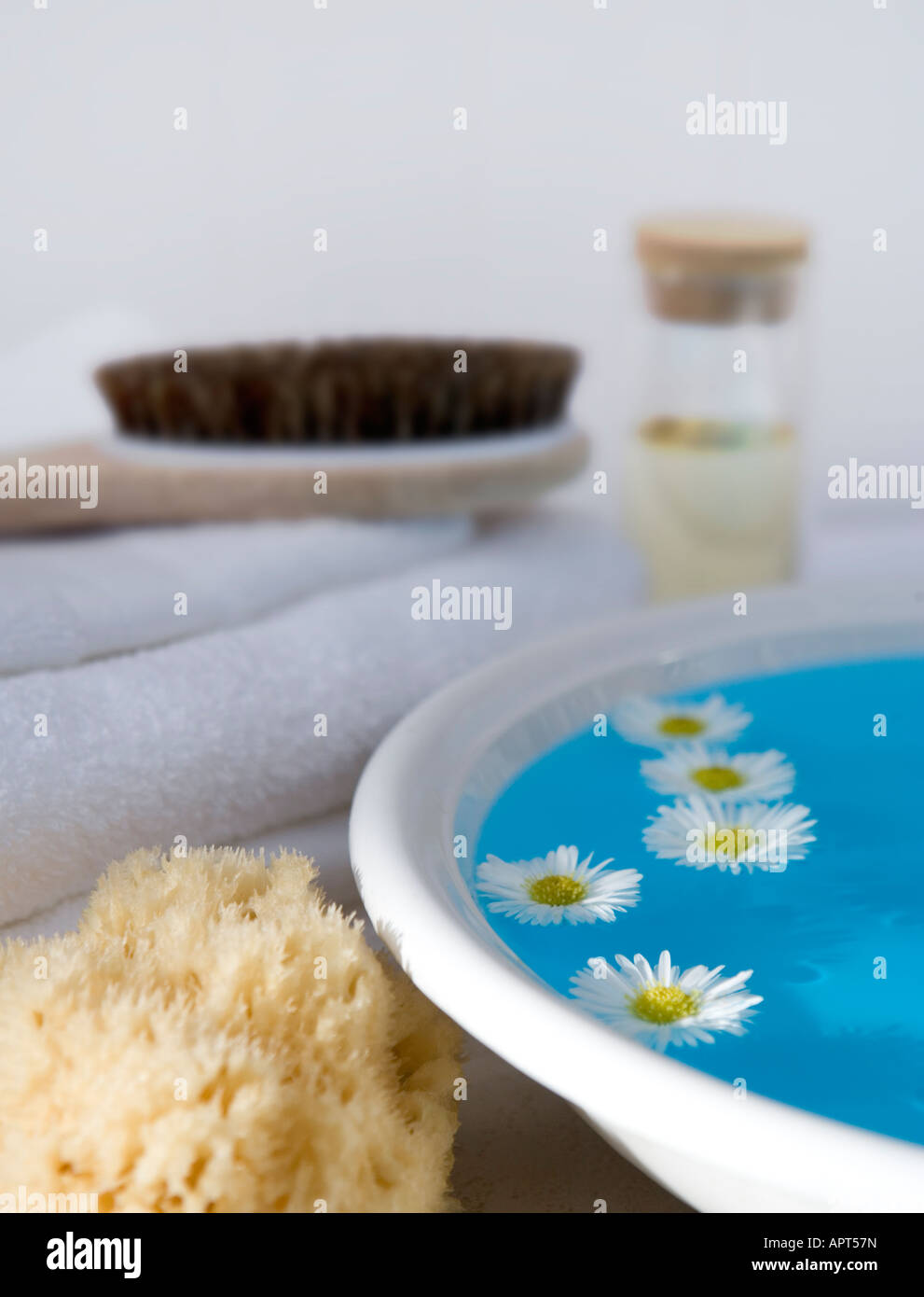 Schüssel mit Wasser mit schwimmenden Blumen, Körperbürste, Naturschwamm und weiße Handtücher Stockfoto