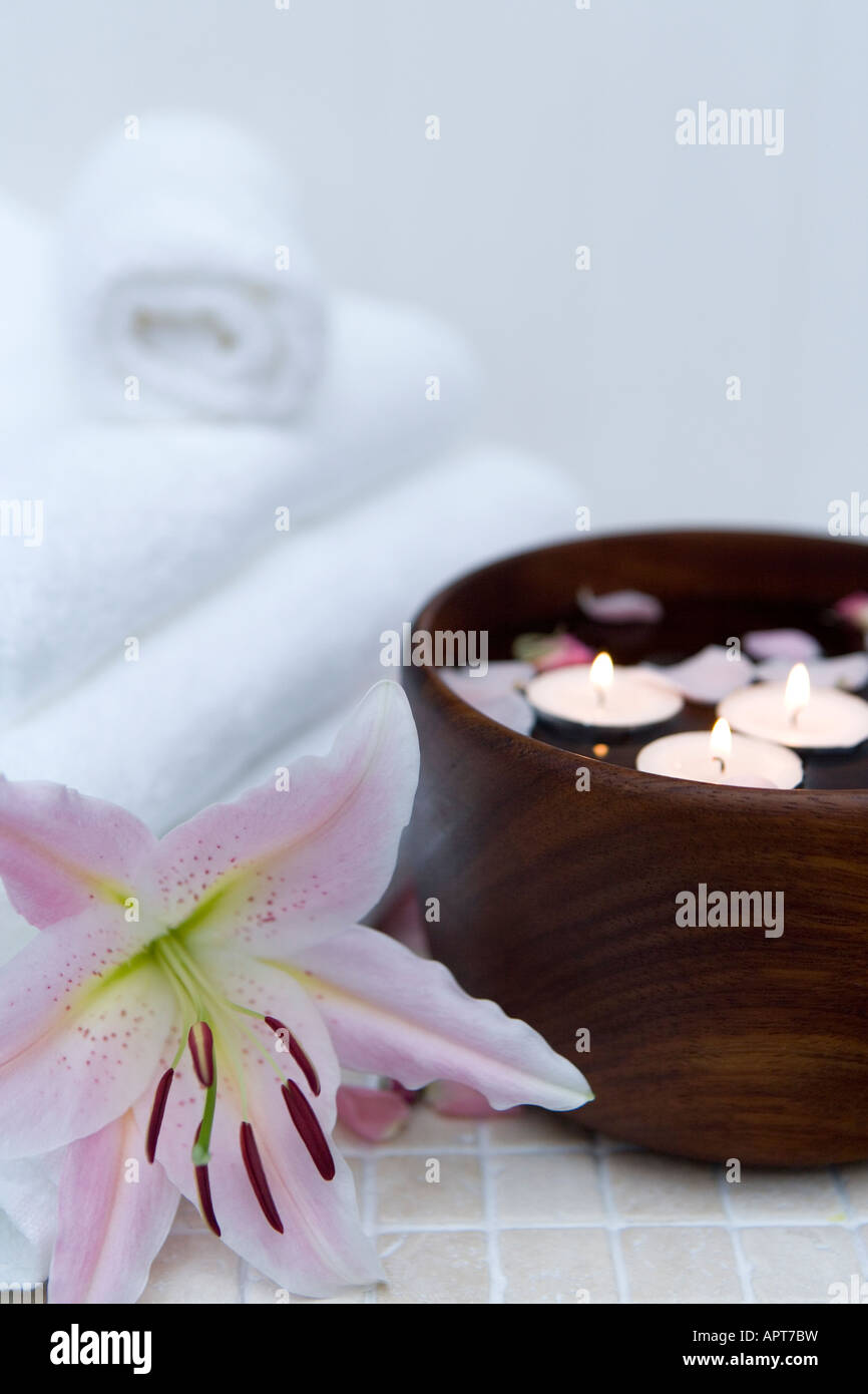 Spa-Einstellung mit schwimmenden Kerzen und Rosenblätter mit Bio weiße Baumwollhandtücher und eine duftende Lilie Blume Stockfoto