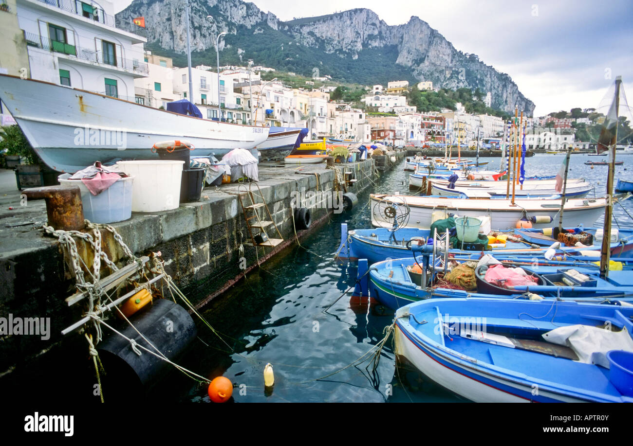 Gozzi Boats Marina Grande Waterfront Capri Italien // CAPRI, Italien - traditionelle Holzboote, die am Ufer von Marina Grande vor Anker liegen. Die farbenfrohen Schiffe, bekannt als gozzi, schweben im kristallklaren Wasser des Hafens, mit den malerischen Gebäuden der Insel im Hintergrund. Stockfoto