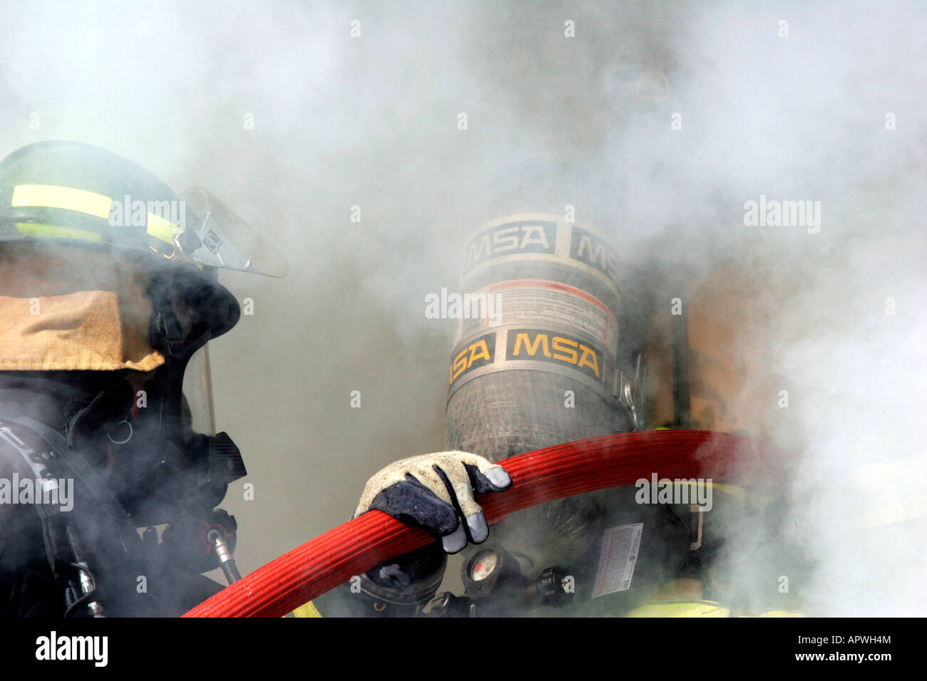 Zwei Feuerwehrleute mit einem Neuanschluß Eingabe Rauch wogenden aus einem Struktur-Feuer Stockfoto