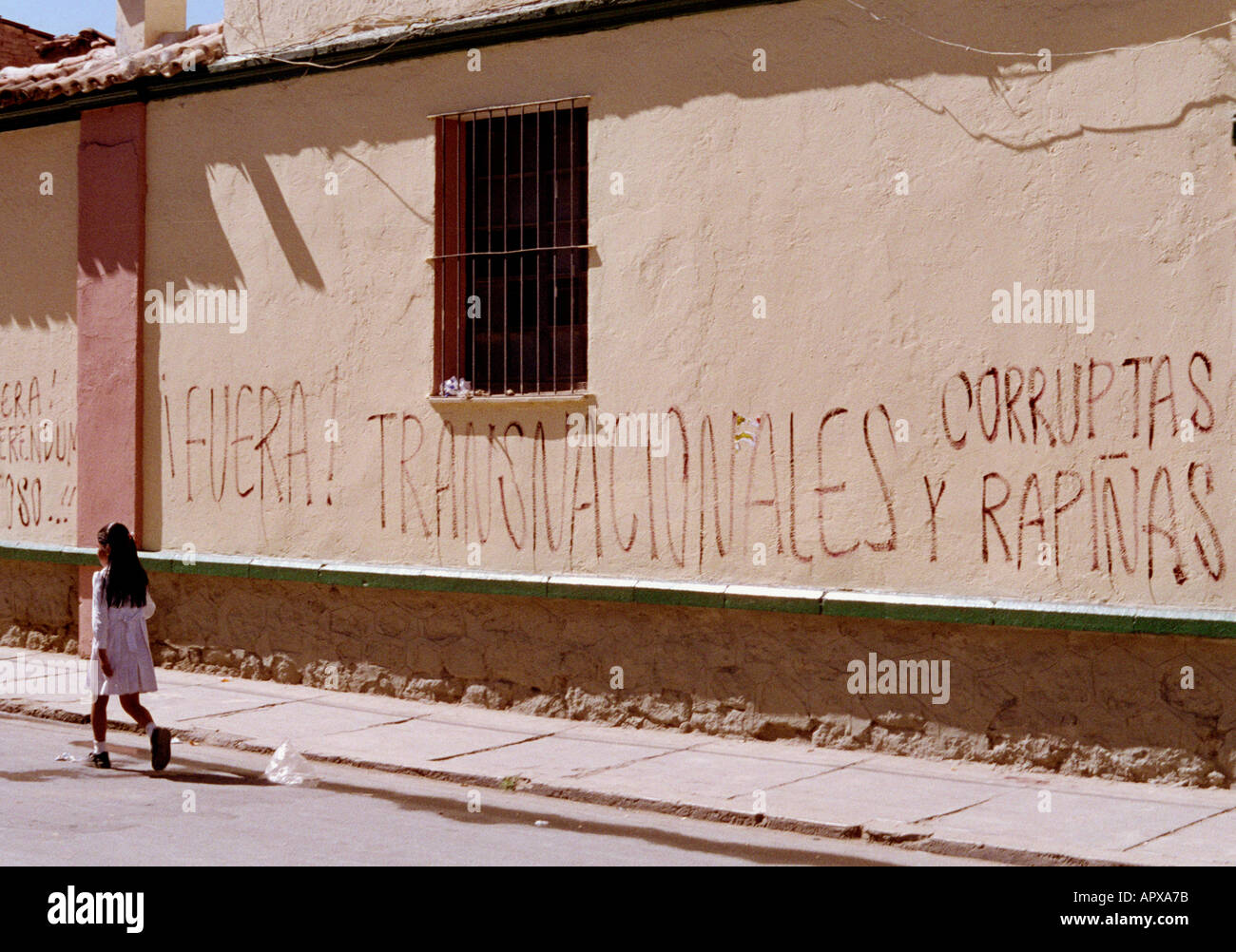 Kleinkind in Kleinstadt in Bolivien mit Fototapete Spruch raus multinationalen korrupte Räuber. Stockfoto
