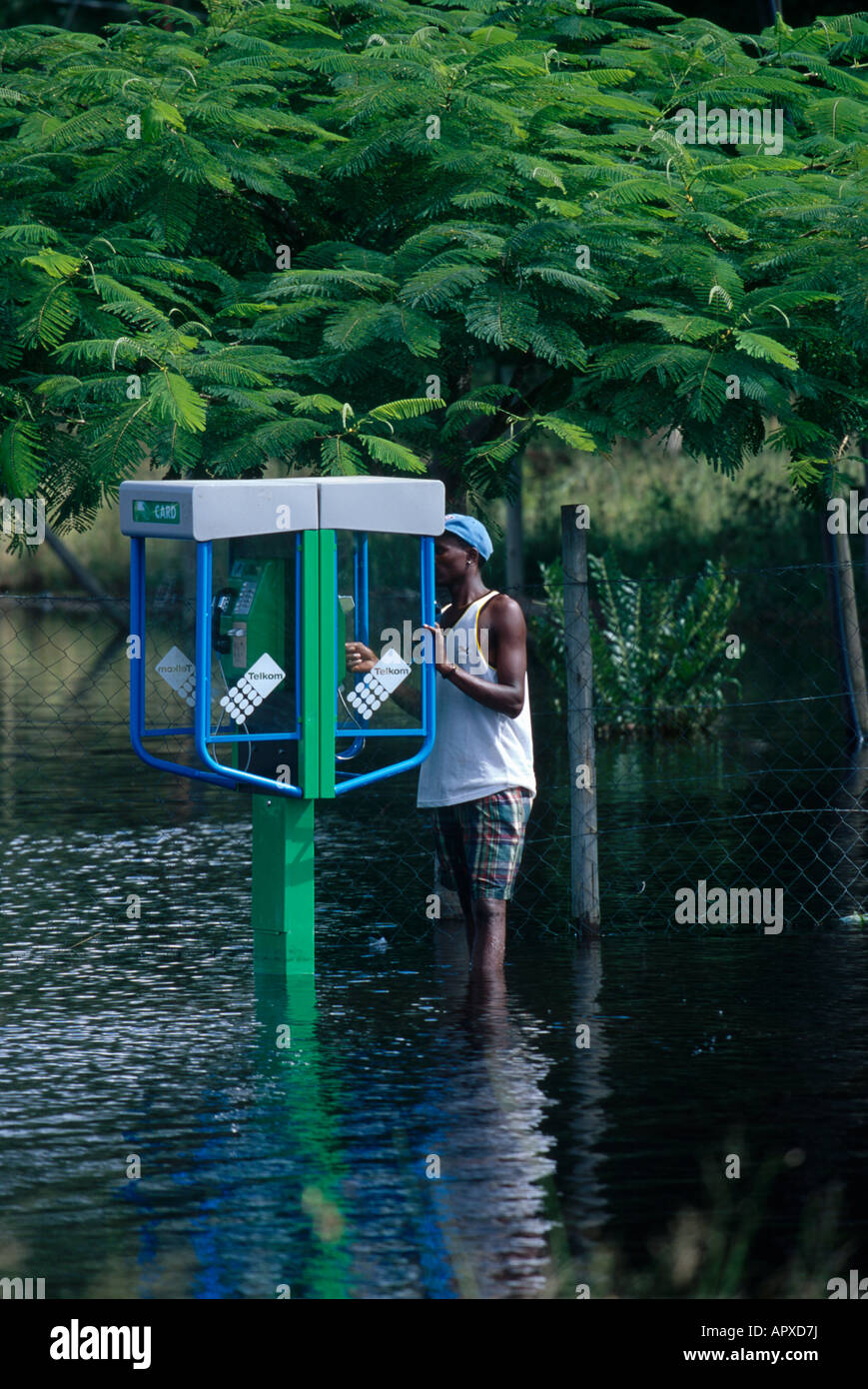 Ein Mann versucht, eine Telkom-Telefonzelle in einer überfluteten Straße zu verwenden Stockfoto