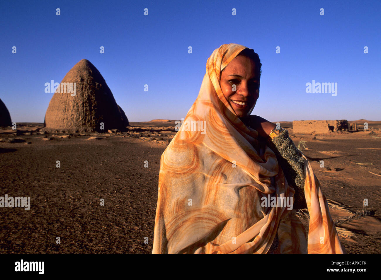Eine nubische Frau in eine orange und gelb gemustertes Kleid steht in der Nähe der Kuppelbauten in Old Dongola Stockfoto