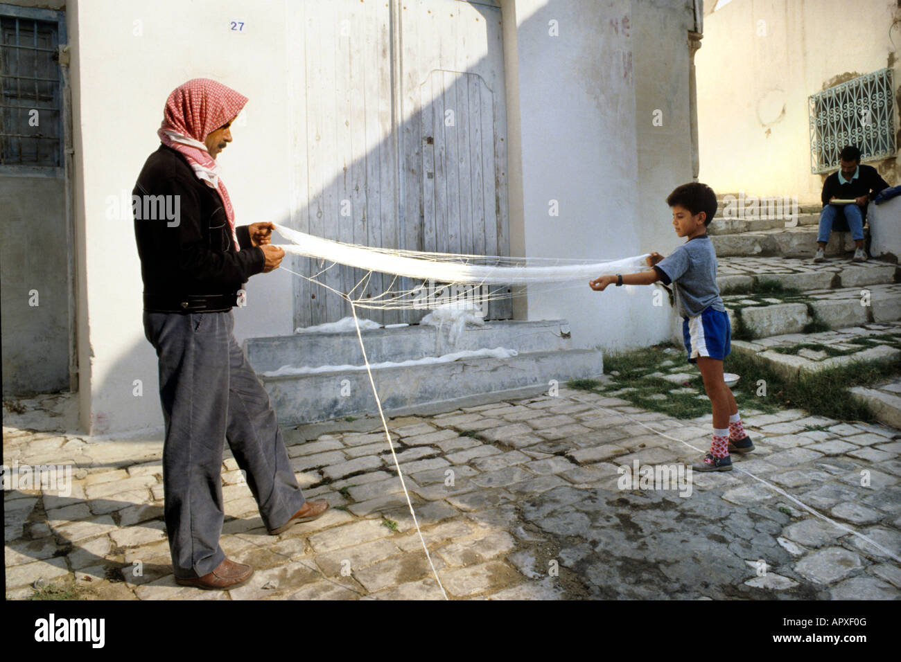 Berber Mann trägt rot gemustert, Kopftuch und seinem kleinen Sohn auf einem Netz zusammenarbeiten Stockfoto