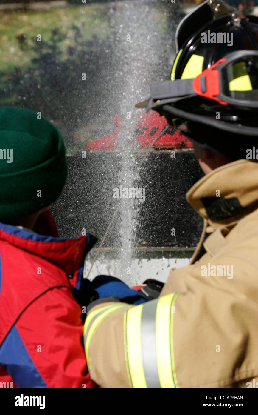 Mequon Feuerwehr Feuerwehrmann und ein kleiner Junge mit einem Neuanschluß Spritzwasser auf ein Haus Feuer Demo Stockfoto