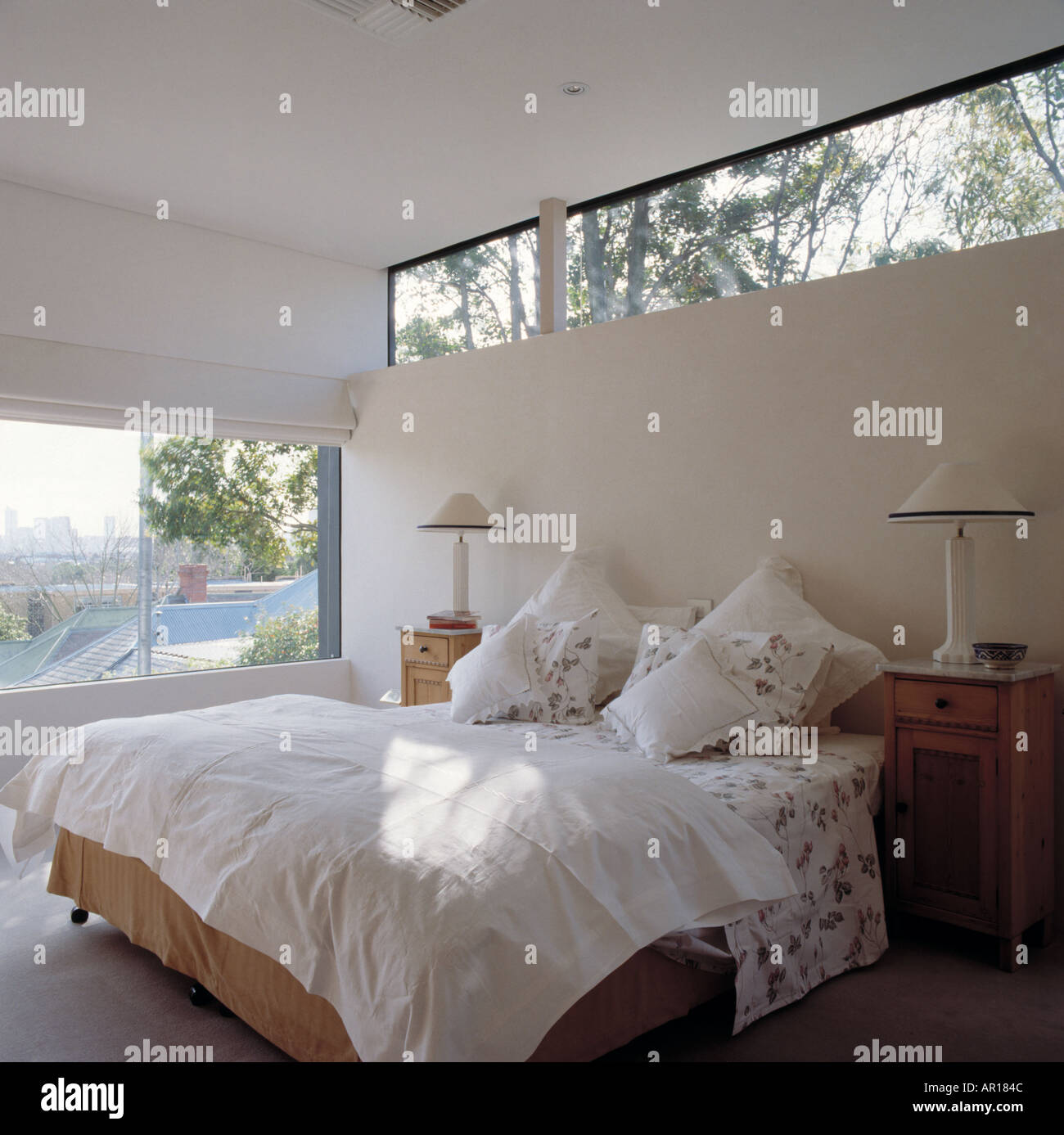 Schmale Fenster über dem Bett mit weißen Kissen und Quilt in hellen und luftigen moderne Schlafzimmer mit weißen Lampen auf Nachttischen Stockfoto