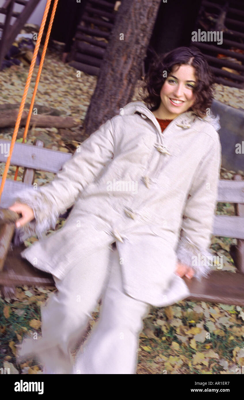 Outdoor-Tag Herbst Gartenschaukel Sway Frau junges Mädchen 20 25 Brünette locken Haare sitzen Rest entspannen Lächeln Lächeln Mantel weiße Spaß Bl Stockfoto