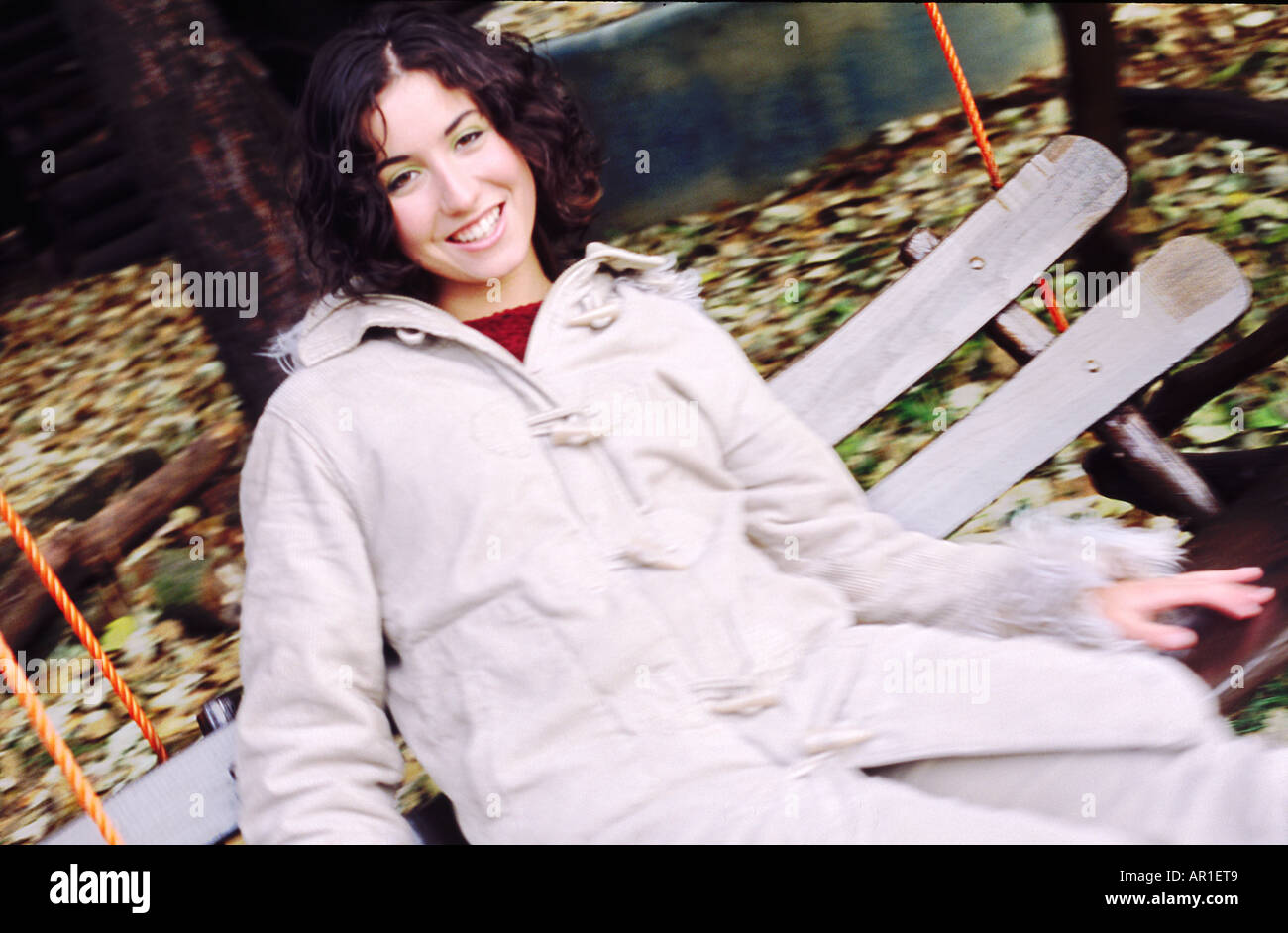 Outdoor-Tag Herbst Gartenschaukel Sway hautnah Frau junges Mädchen 20 25 Brünette locken Haare sitzen Rest entspannen Lächeln Lächeln Mantel whi Stockfoto