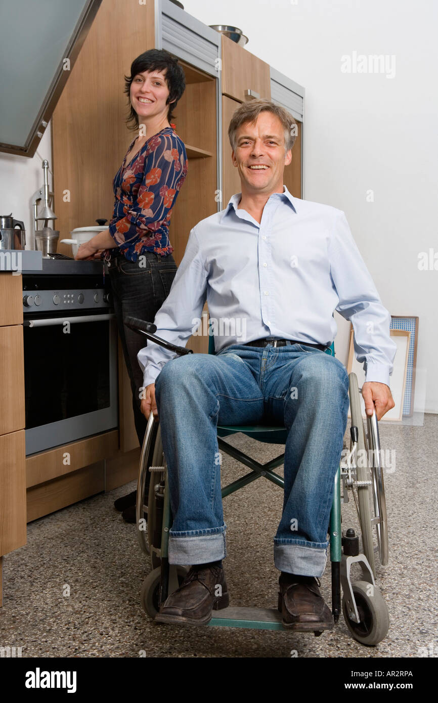 Mann sitzt im Rollstuhl und Frau hinter im heimischen Küche Stockfoto