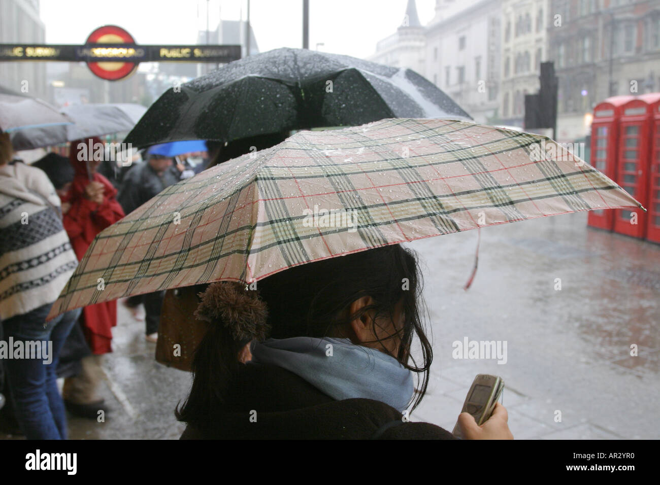 Eine Frau prüft ihr Mobiltelefon einen Regenschirm halten, während ein starker Regenguss Regen, Tottenham Court Road, London, UK. 2006. Stockfoto