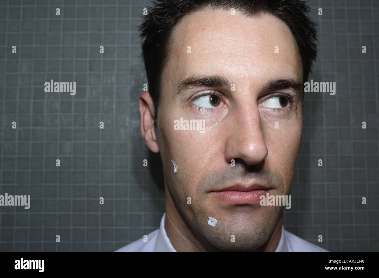 Porträt eines jungen Geschäftsmann mit Rasierschnitten und Gewebe im Gesicht im Badezimmer Stockfoto
