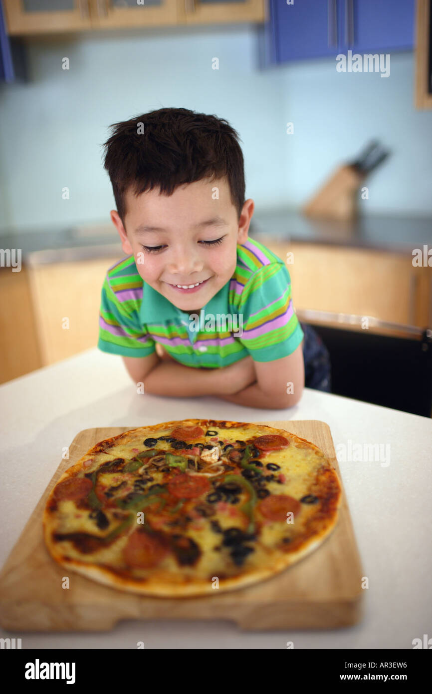 Kleiner Junge betrachtet man gekochte Pizza am Küchentisch Stockfoto