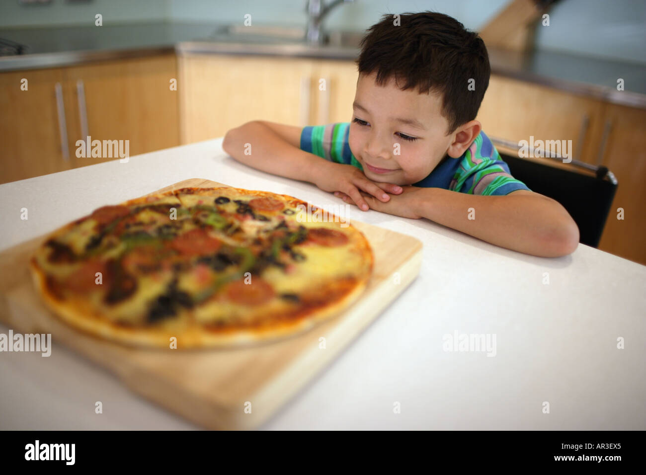 Kleiner Junge betrachtet man gekochte Pizza am Küchentisch Stockfoto