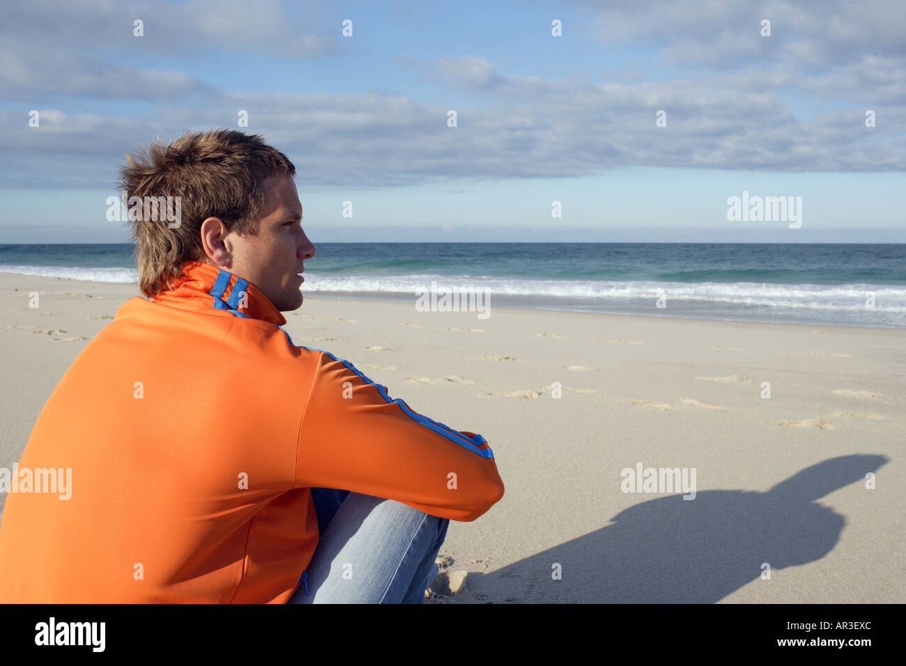Junger Mann sitzt am Strand mit Blick auf das Meer Stockfoto