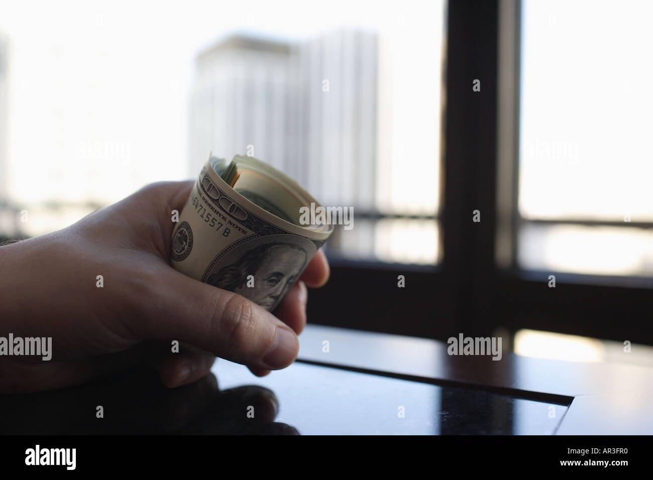 Männliche Hand hält eine gerollte Bündel von US-Dollar auf executive Tisch Stockfoto