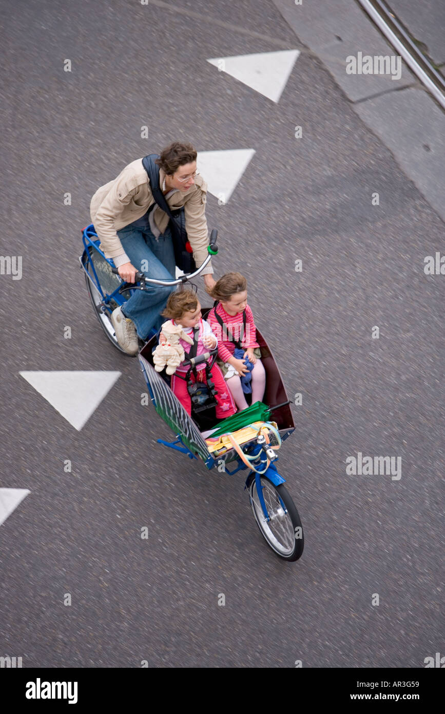 HOLLAND-AMSTERDAM-MUTTER MIT ZWEI KINDERN AUF EINEM CARGOBIKE RADFAHREN ÜBER WEIßE DREIECKE ZEICHEN AUF DIE STRAßE GEMALT Stockfoto