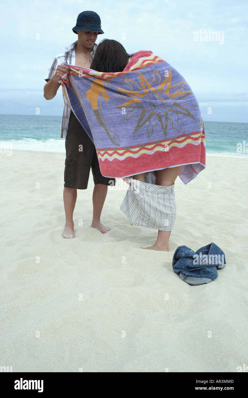 Junges Mädchen mit Strandtuch gehaltenen junger Mann versucht zu erhalten geändert am Strand Stockfoto