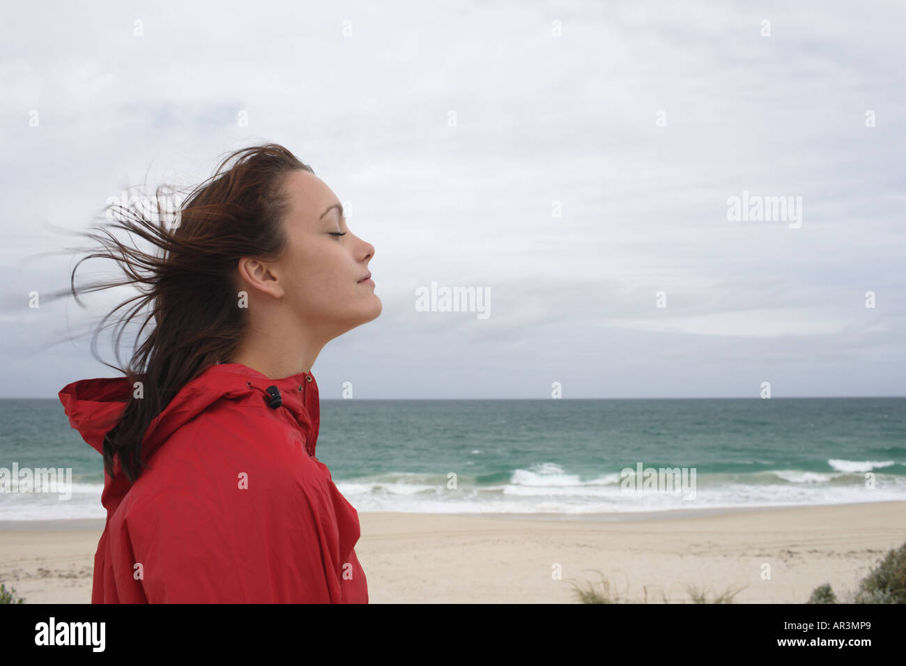 Junge Frau trägt rote Regenmantel am Strand Stockfoto