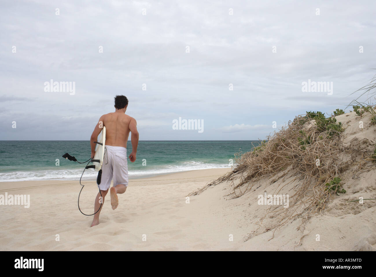 Junger Mann mit Surfbrett Strand entlang laufen Stockfoto