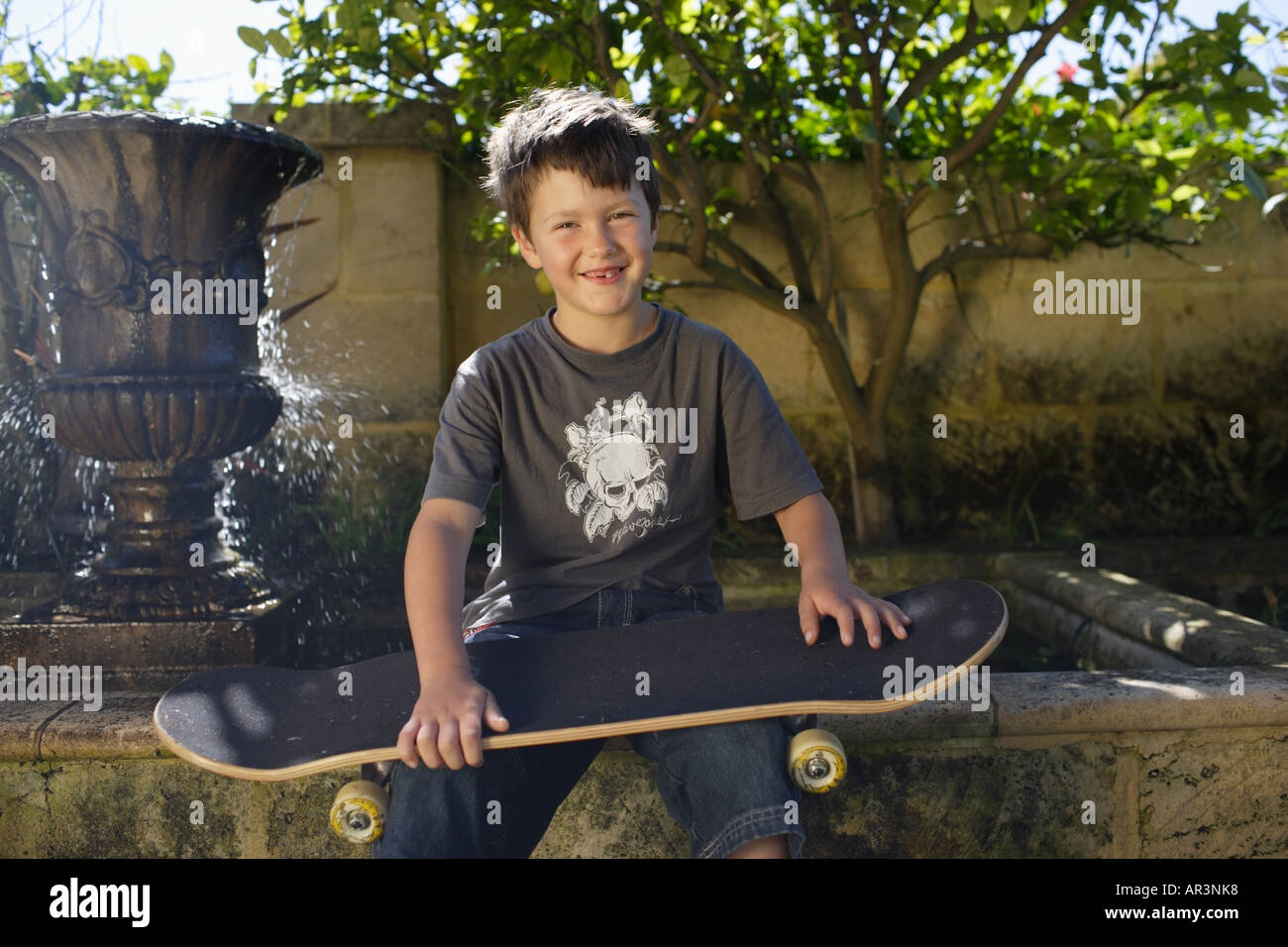Kleiner Junge sitzen im Garten mit Skateboard, Lächeln Stockfoto