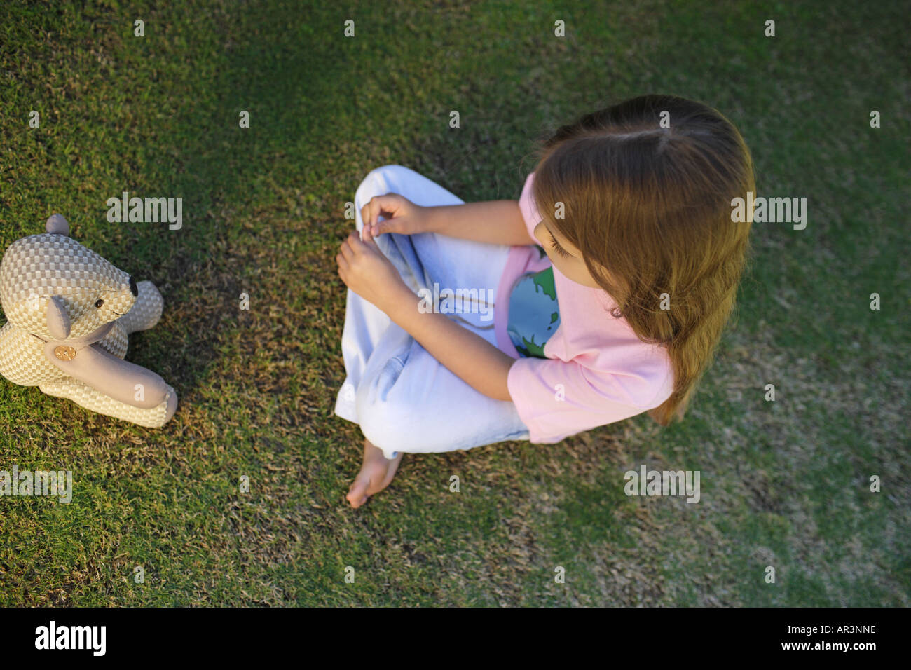 Junges Mädchen sitzen auf dem Rasen gegenüber Spielzeug Bär Stockfoto