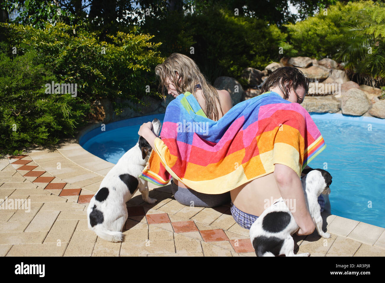 Junges Paar mit Haustier Hunde sitzen seitlich der Außenpool mit Handtuch Stockfoto