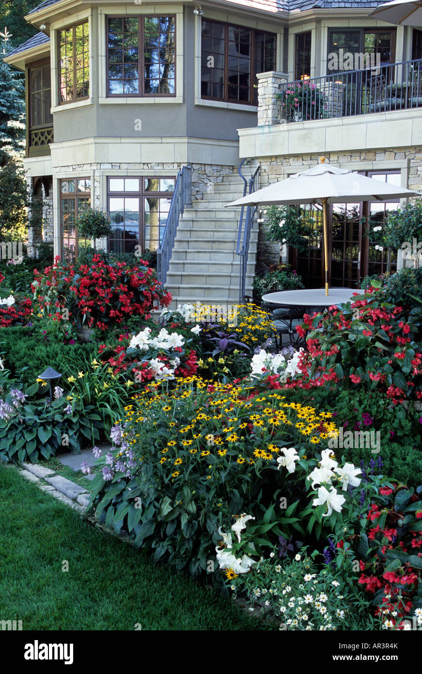 RÜCKANSICHT DES LUXUS-MINNESOTA-HAUS MIT TERRASSE UND GARTEN GRENZE VON EINJÄHRIGEN PFLANZEN UND STAUDEN.  MITTEN IM SOMMER.  VEREINIGTE STAATEN VON AMERIKA Stockfoto