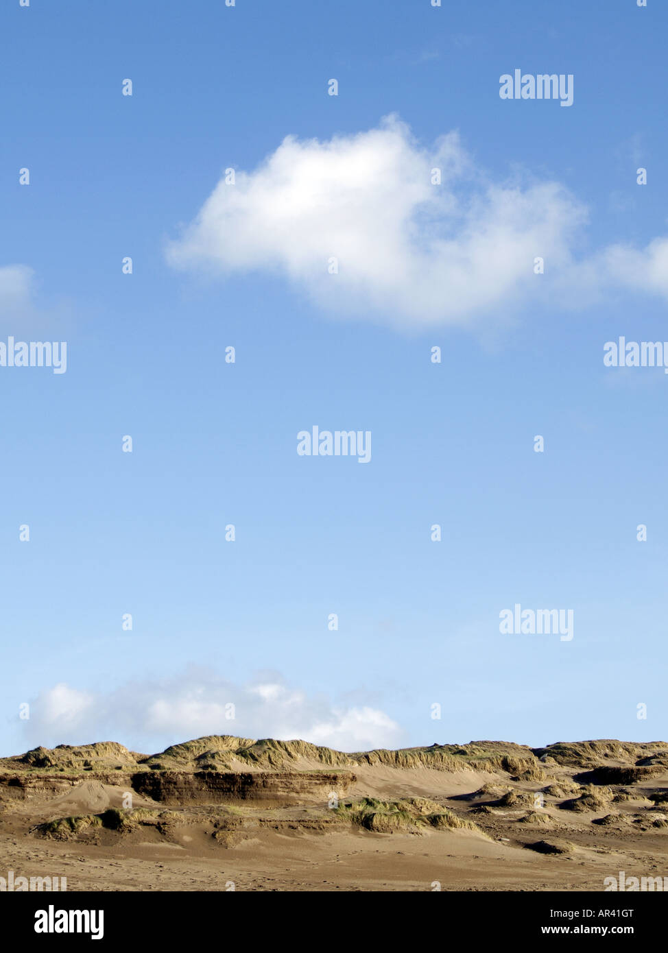Klarer blauer Himmel mit flauschigen weißen Wolken über Sanddünen Stockfoto
