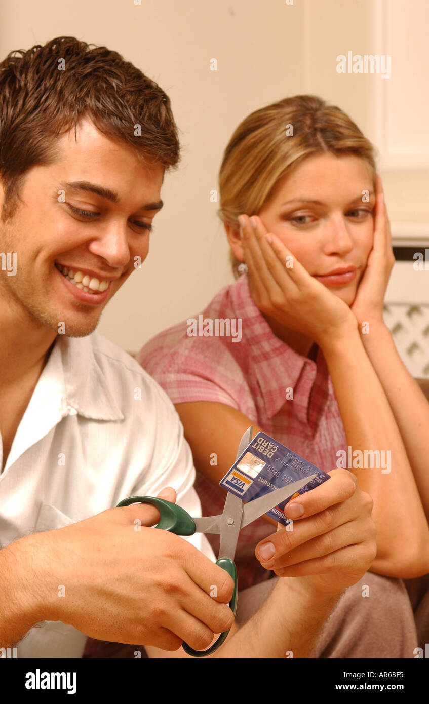 Paar, sitzen auf dem Sofa männlich auf Vordergrund links kurze Kastanien welliges Haar weißen kurzen Ärmeln t-Shirt zerschneiden Kreditkarte Stockfoto