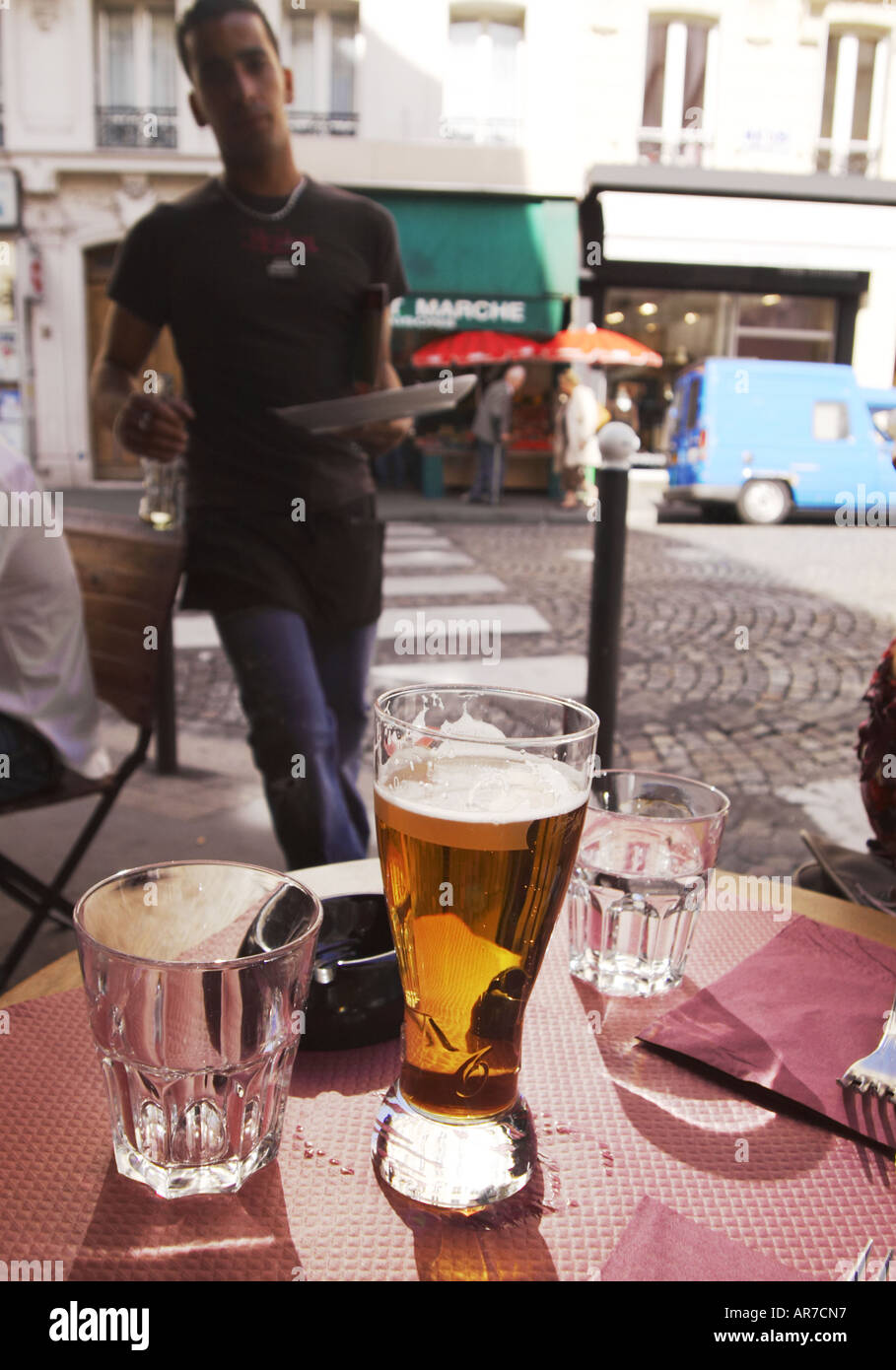 ein Glas Bier auf einem Straßencafé Tisch auf Rue des Abbesses Montmartre Paris Kellner mit Tablett im Hintergrund Stockfoto