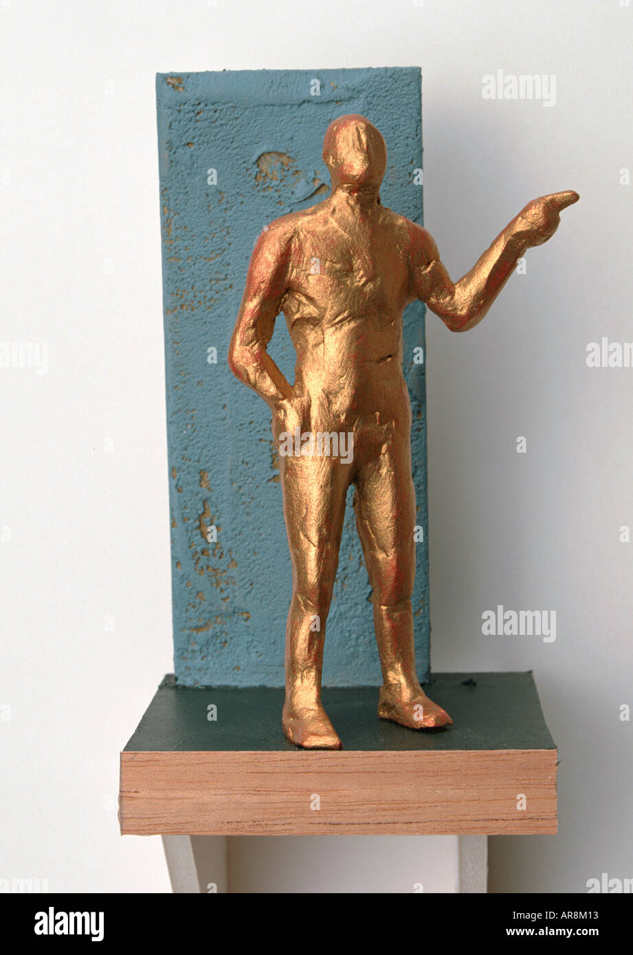 Goldene menschliche Figur stehend hoch und zeigt mit dem Zeigefinger, andererseits an Hüfte, durchsetzungsfähig Haltung vor blauem Hintergrund. Stockfoto Goldene menschliche Figur stehend hoch und zeigt mit dem Zeigefinger, andererseits an Hüfte, durchsetzungsfähig Haltung vor blauem Hintergrund. Stockfoto