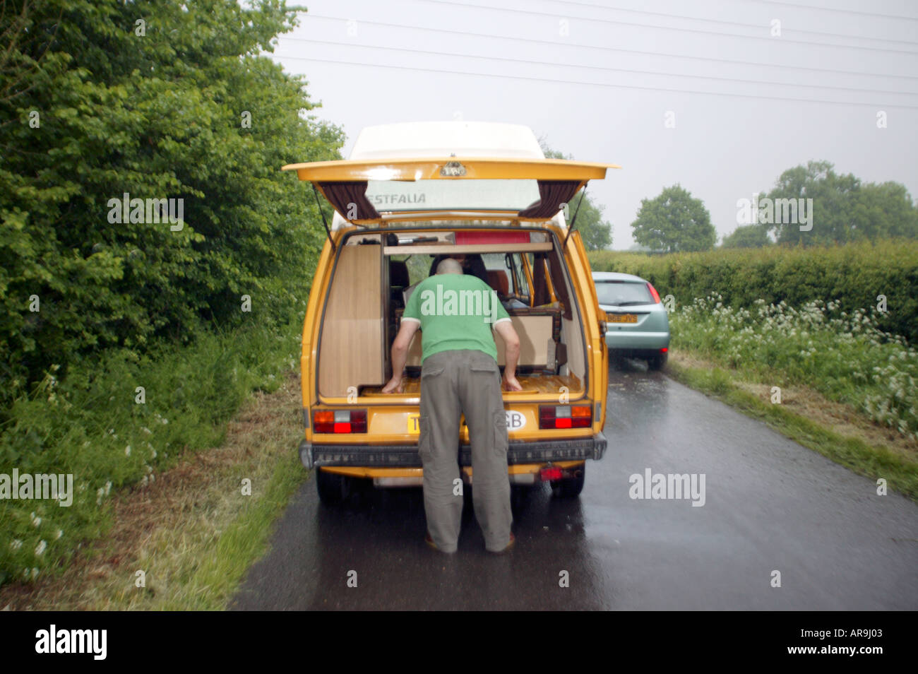 Mann sucht am Motor auf der Rückseite gelb Vw Camper van in der englischen Country Lane Volkswagen Stockfoto