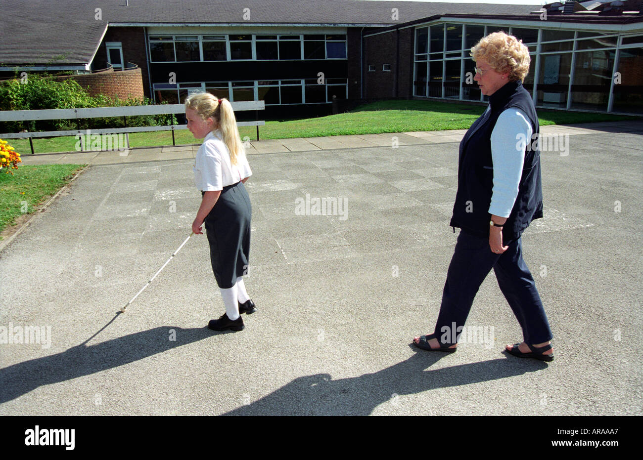 Junge sehbehinderte Schule Mädchen mit Zuckerrohr von Mitarbeitern der Schule Mitglied an einer Schule, Midlands, England beschattet. Stockfoto