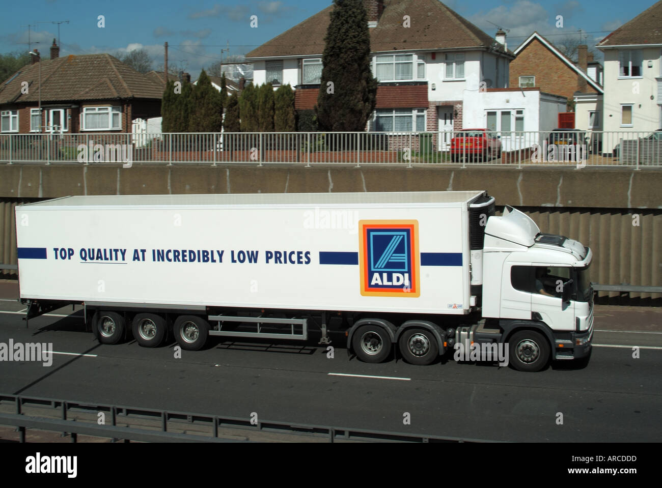 Aldi Supermarkt LKW auf Bundesstraße in Schneiden unter Wohngebäude mit separaten Zufahrtsstraße zeigt Stützmauer Stockfoto