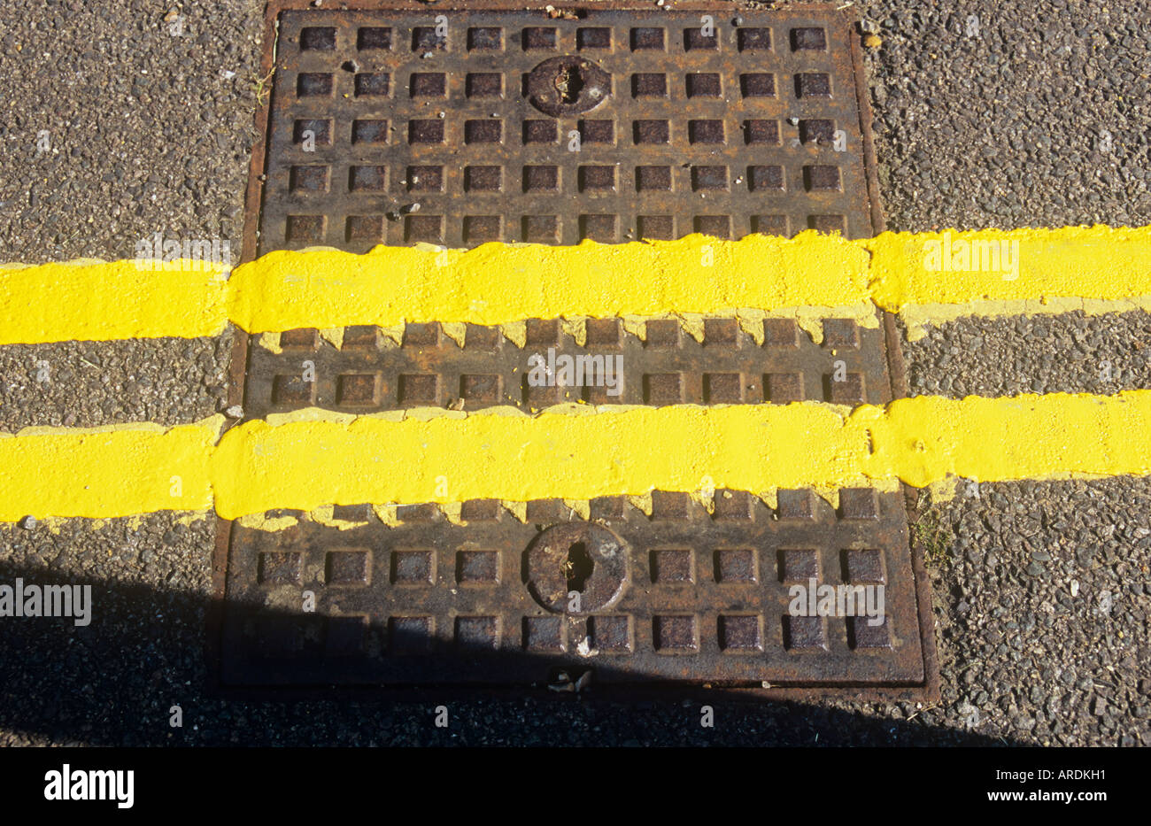 Detail von oben der frisch gestrichene doppelte gelbe Linien kreuzen ein Quadrat Metall Schachtdeckel inmitten einer Asphaltstraße Stockfoto