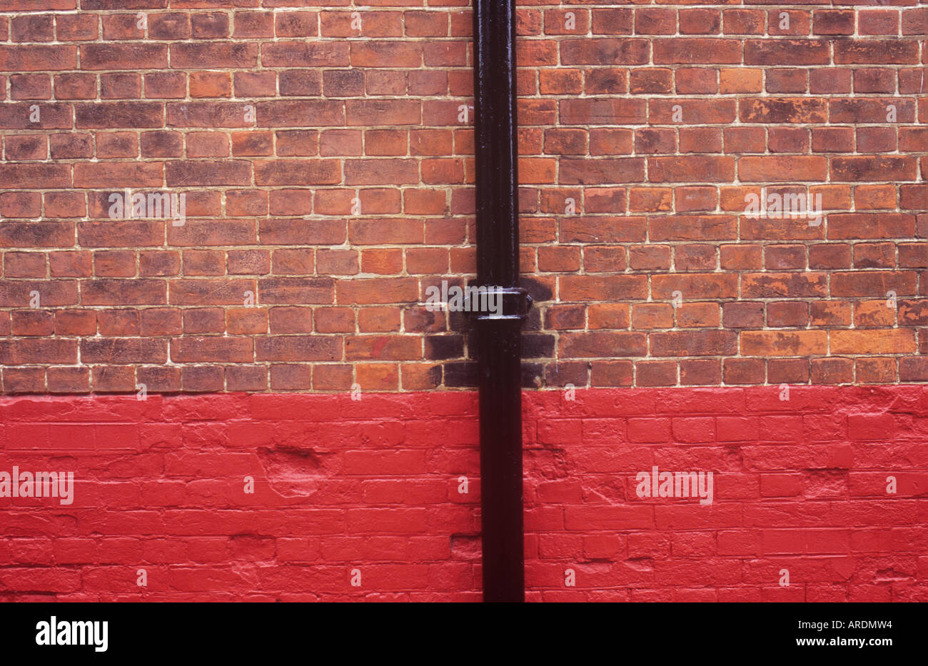 Detail des dunklen roten Brickwall im untere Drittel davon ein frisches rot gemalt worden ist und mit einem neu lackiert Schwarz Fallrohr Stockfoto