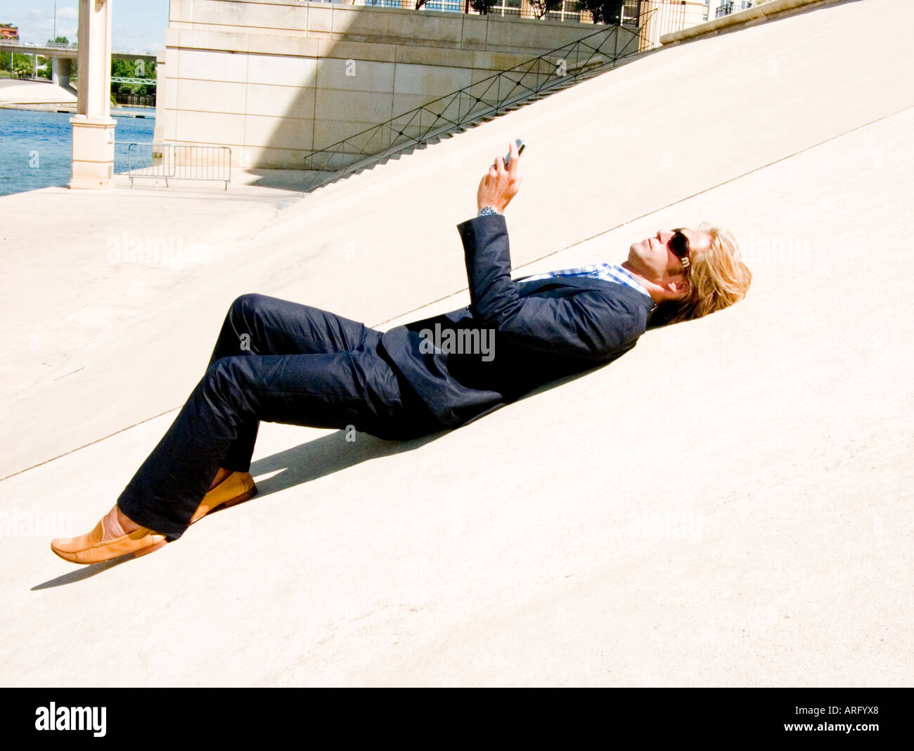 Ein junger kaukasischen Geschäftsmann mit Blackberry auf eine konkrete Steigung in der Sonne liegen Stockfoto