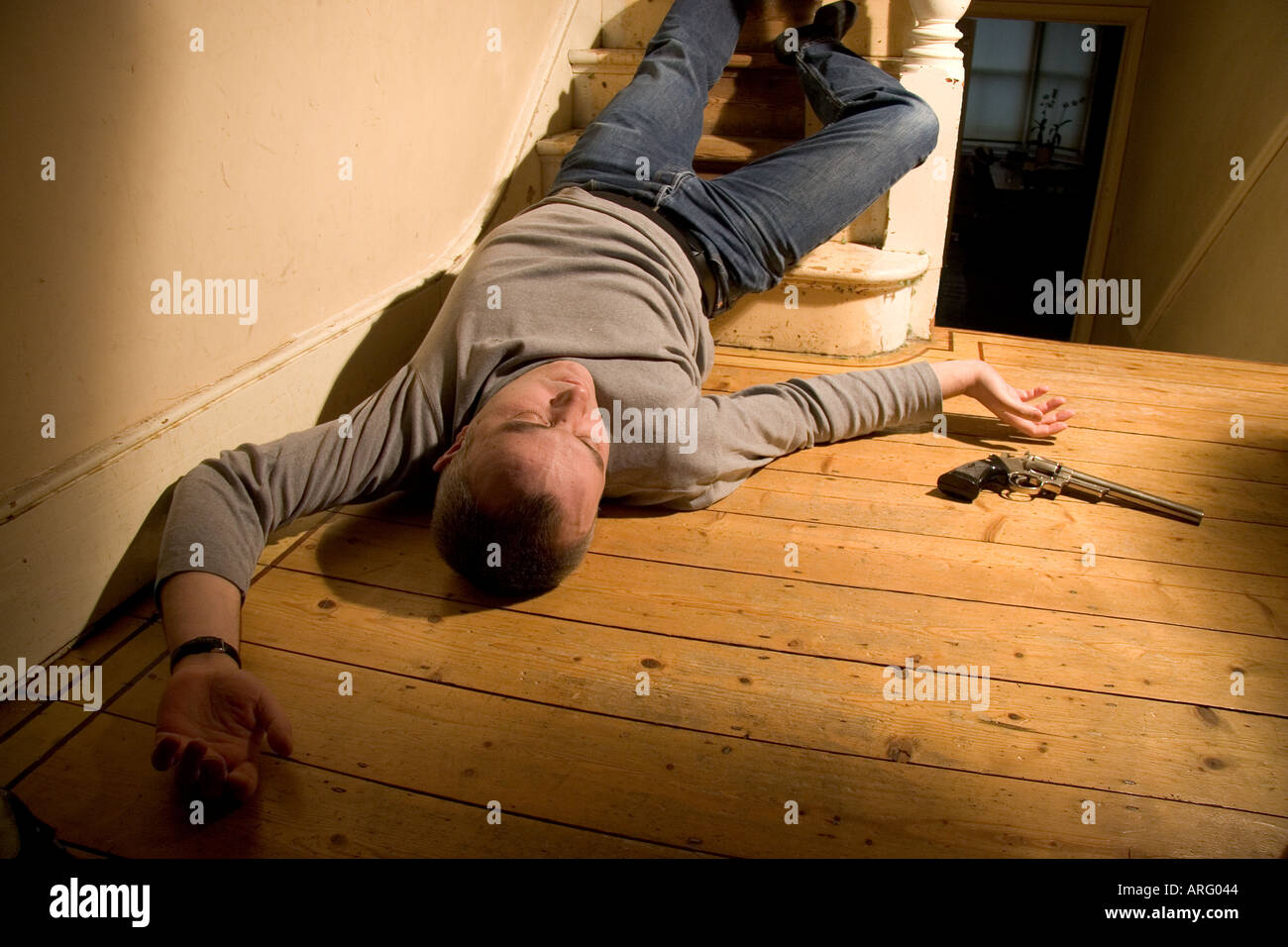 Körper des toten Mannes auf dem Boden an der Unterseite der Treppe mit einer Pistole an seiner Seite liegend Stockfoto