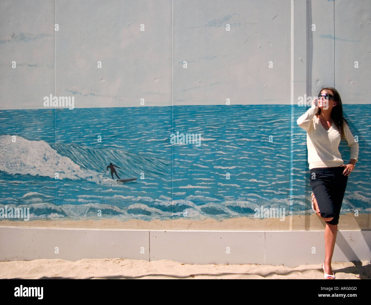 einem niedrigen Winkel Schuss junge Frau gelehnt ein Wandbild des Surfers auf Welle sprechen auf ihrem Handy Stockfoto