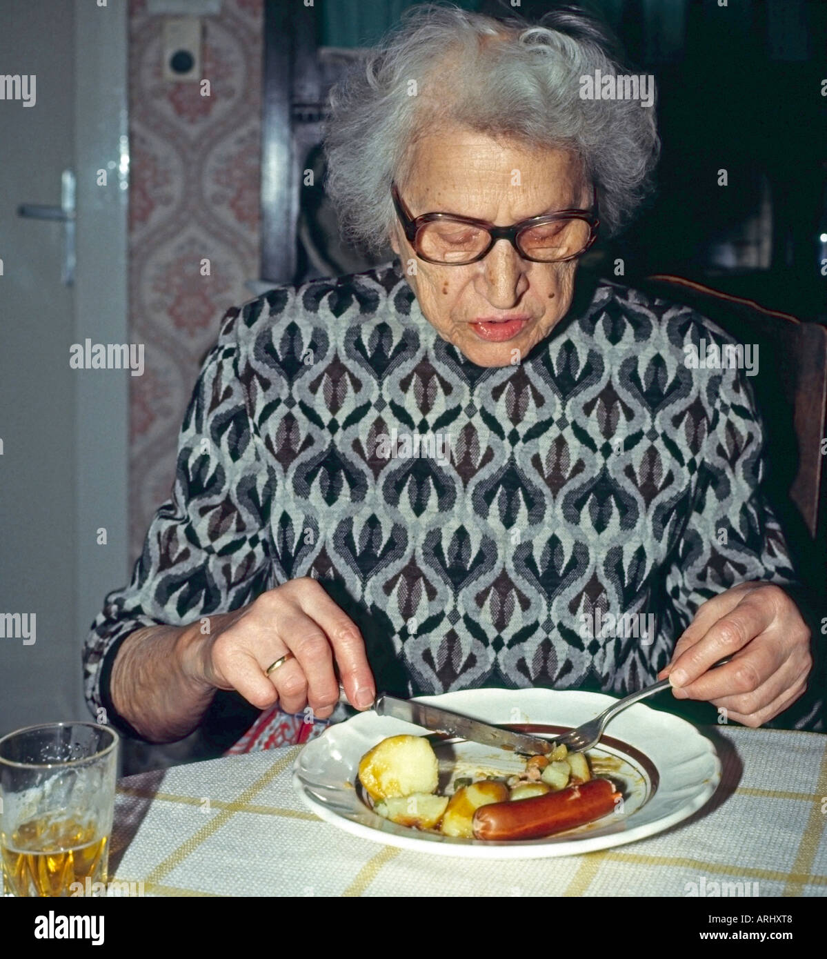 alte Frau allein zu Hause an einem Tisch essen Würstchen und Kartoffeln Stockfoto