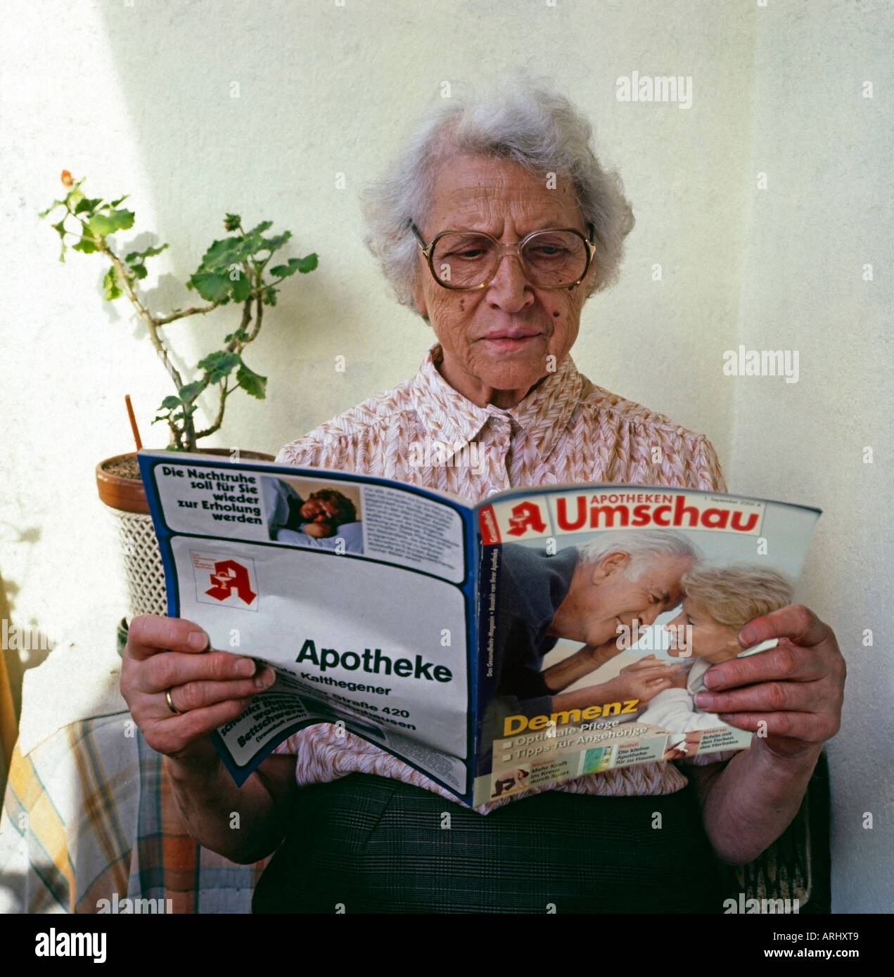 alte Frau sitzt auf Balkon lesen ein Magazin aus der Apotheke mit einem Berichtartikel über Demenz Stockfoto